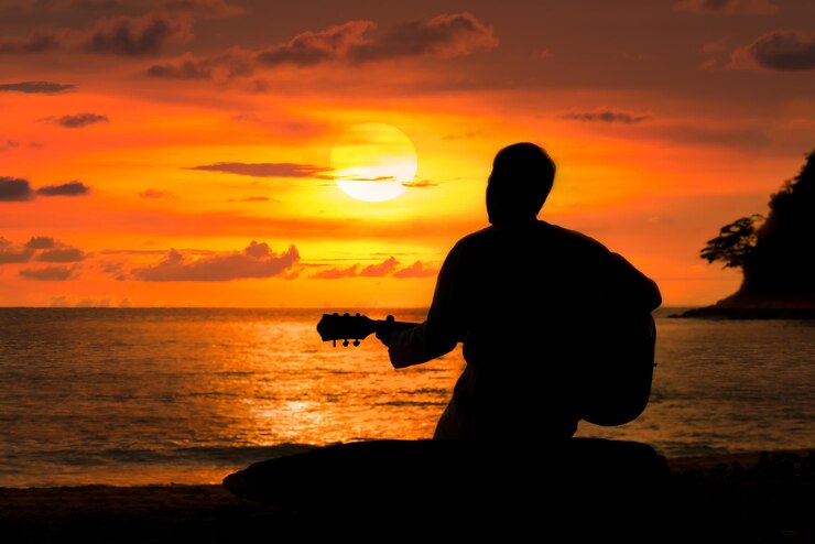Foto uomo a silhouette che suona la chitarra sulla spiaggia contro un cielo arancione