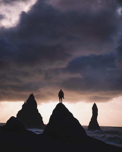 Uomo a silhouette in piedi su una roccia sulla spiaggia contro il cielo durante il tramonto