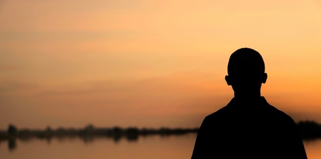 Uomo a silhouette in piedi vicino al lago contro il cielo durante il tramonto