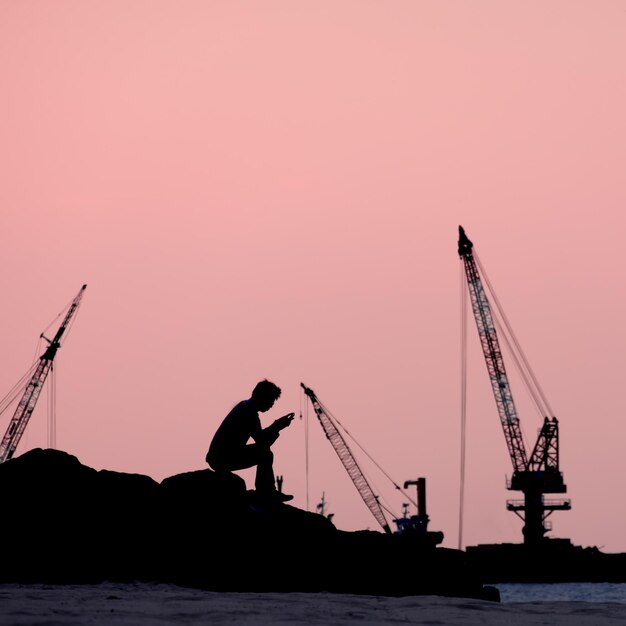 Uomo a silhouette seduto su una roccia sulla spiaggia contro il cielo durante il tramonto