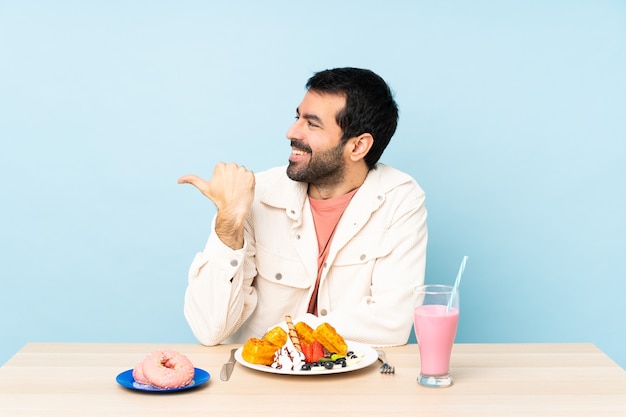 Uomo a un tavolo con cialde per la colazione e un frappè che punta di lato