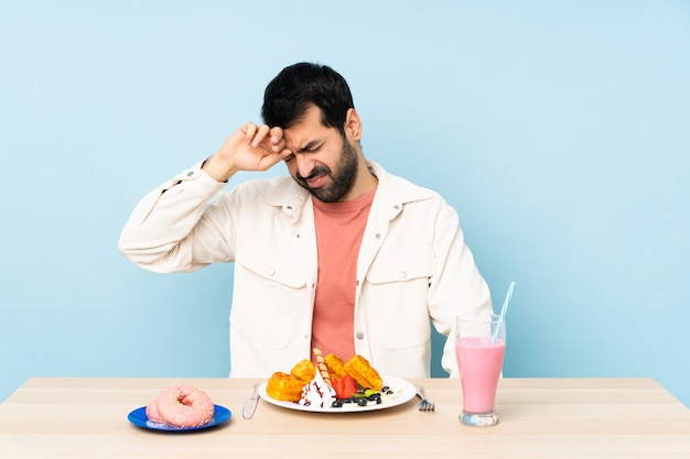 Uomo a un tavolo con cialde per la colazione e un frappè con espressione stanca e malata