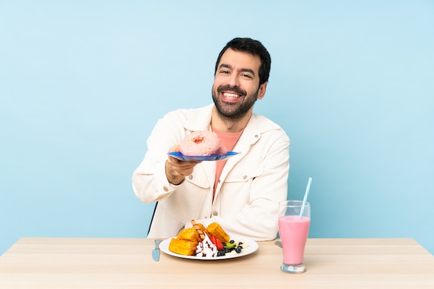 Uomo a un tavolo con cialde per la colazione e un frappè