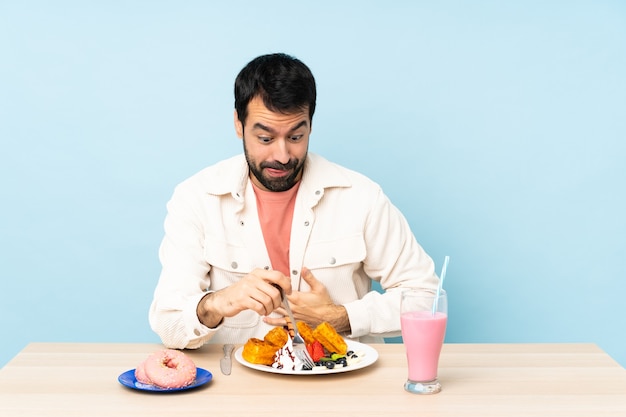 Uomo a un tavolo con cialde per la colazione e un frappè