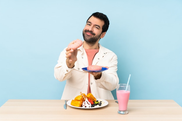 Uomo a un tavolo con cialde per la colazione e un frappè