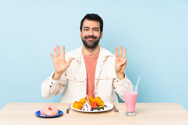 Uomo a un tavolo con cialde per la colazione e un frullato contando otto con le dita