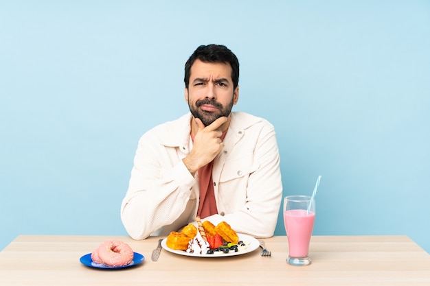 Uomo a un tavolo con cialde per la colazione e un pensiero frappè