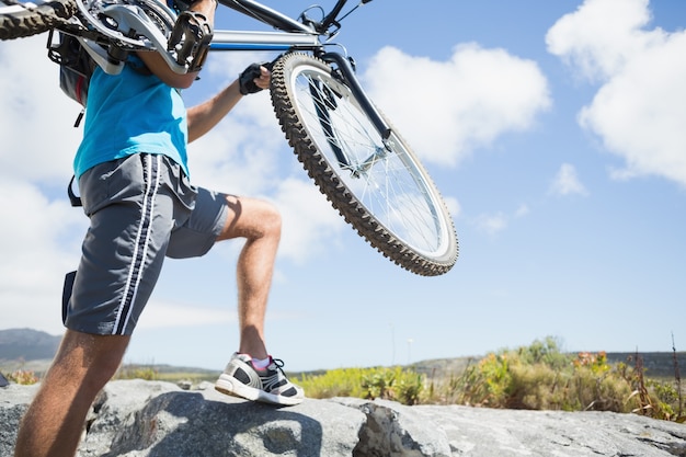 Uomo adatto che cammina su terreno roccioso tenendo mountain bike