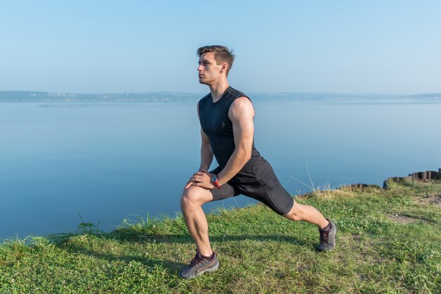 Uomo adatto dei giovani che allunga le gambe all'aperto che fa affondo in avanti.