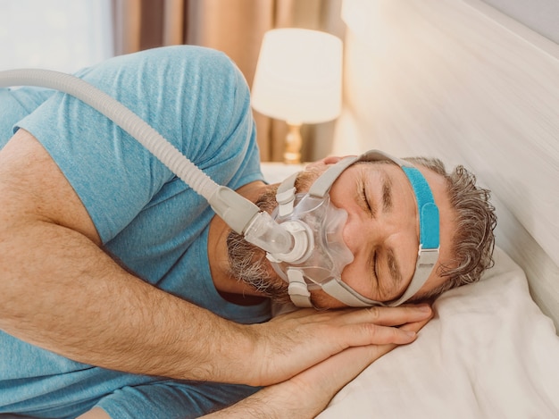 uomo addormentato con problemi respiratori cronici che usa la macchina cpap a letto