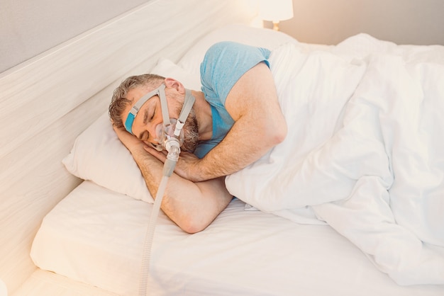 uomo addormentato con problemi respiratori cronici che usa la macchina cpap a letto