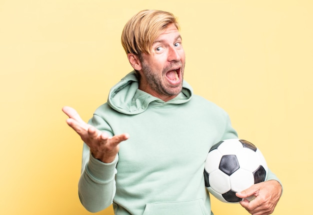 Uomo adulto bello biondo che tiene un pallone da calcio