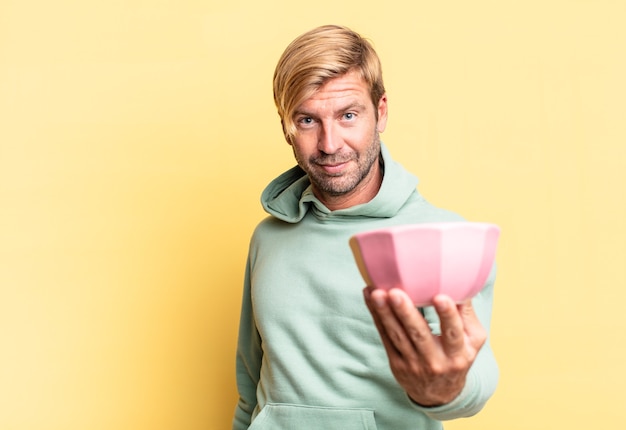 Uomo adulto bello biondo che tiene un vaso vuoto contro il muro giallo