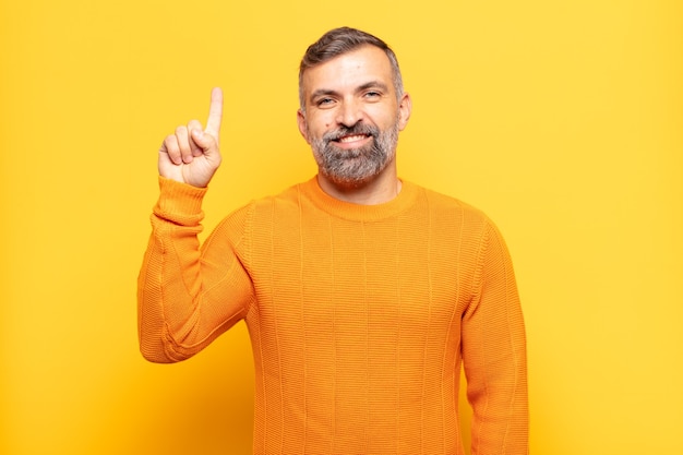 Uomo adulto bello che sorride allegramente e felicemente, rivolto verso l'alto con una mano per copiare lo spazio