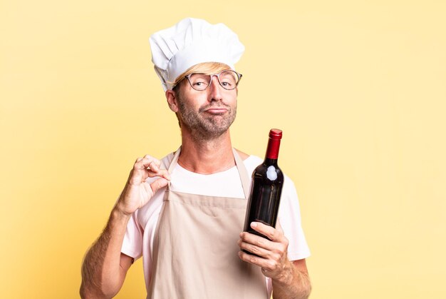 Uomo adulto biondo bello chef che tiene una bottiglia di vino
