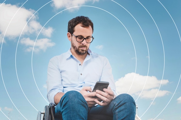 Uomo adulto caucasico su sedia a rotelle, che emette segnali e onde nel cielo, comunica per telefono, comunicazione telefonica globale, affari digitali e comunicazione senza limiti.