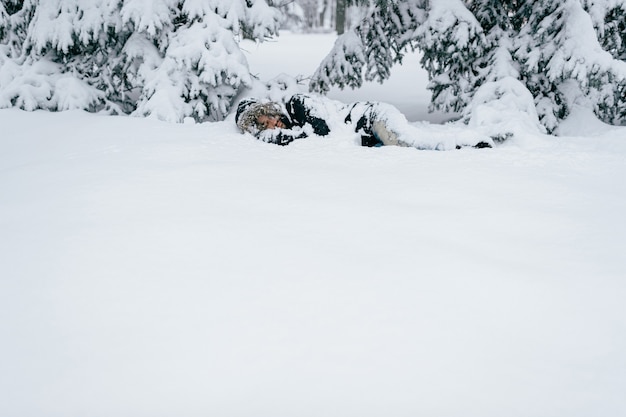 Uomo adulto che dorme sotto gli alberi innevati