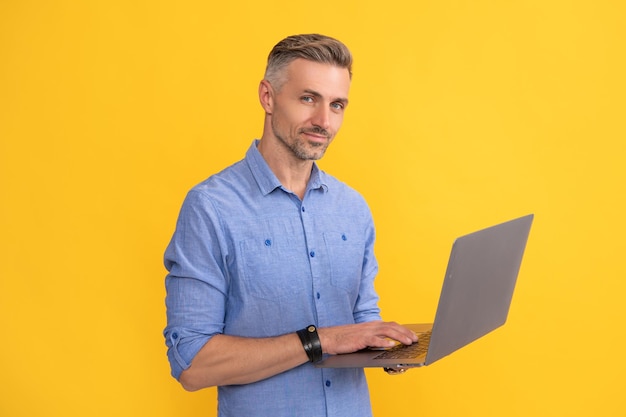 Uomo adulto che lavora online su laptop su sfondo giallo imprenditore
