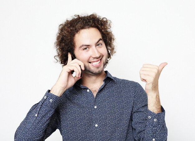 Uomo adulto che parla al telefono in piedi su sfondo bianco facendo segno giusto con le dita simbolo eccellente