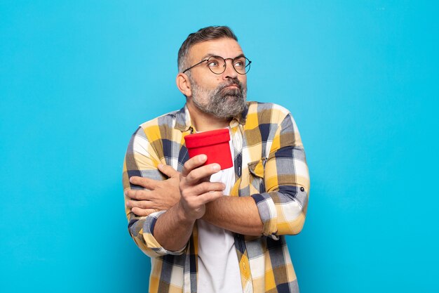 Uomo adulto che scrolla le spalle, sentendosi confuso e incerto, dubitando con le braccia incrociate e lo sguardo perplesso