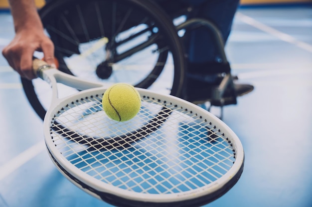 Uomo adulto con disabilità fisica su sedia a rotelle che gioca a tennis su un campo da tennis al coperto