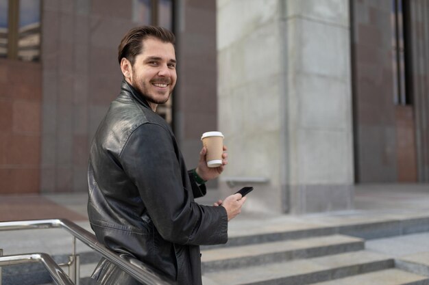 Uomo adulto con una tazza di caffè in mano e un telefono cellulare all'esterno