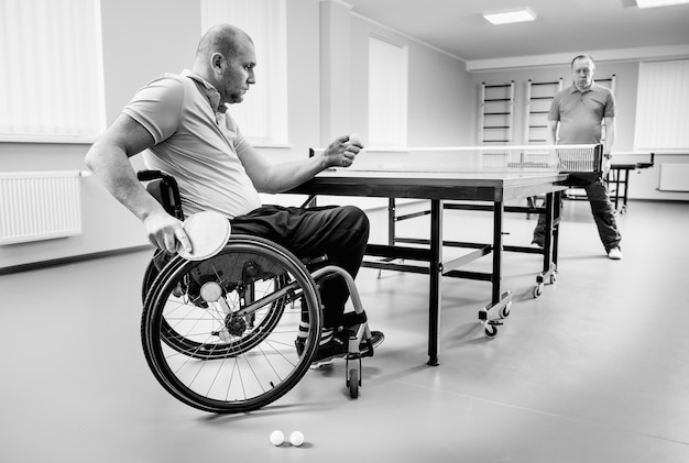 Uomo adulto disabile in sedia a rotelle gioca a ping pong con il suo allenatore