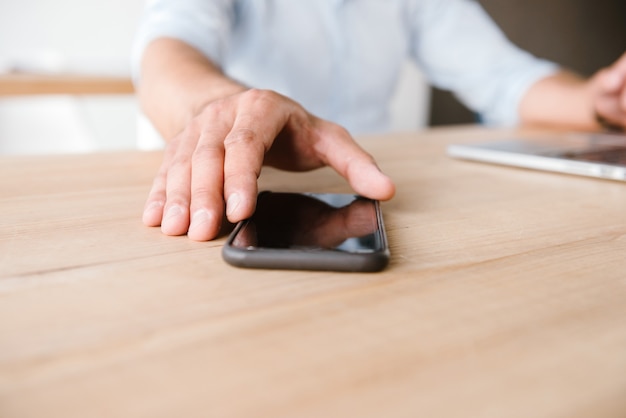 uomo adulto in camicia bianca prendendo il telefono cellulare dal tavolo, mentre è seduto e lavora in ufficio