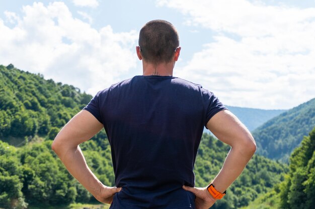 Uomo adulto in piedi di nuovo alla telecamera e guardando le montagne in un giorno d'estate