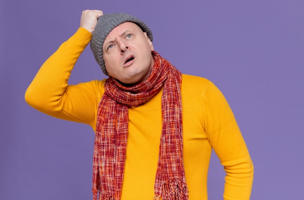 Uomo adulto incapace con una sciarpa intorno al collo che tiene in mano un cappello invernale e guarda in alto