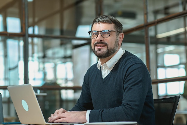 Uomo adulto positivo seduto in ufficio mentre si utilizza il computer portatile