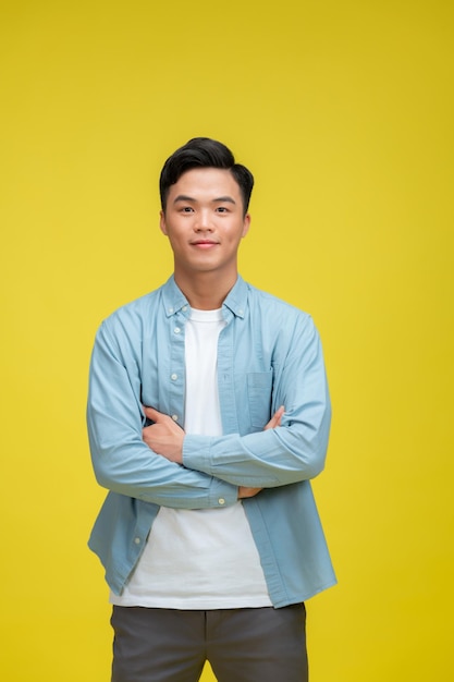 Uomo affascinante sorridente in camicia polo blu in piedi con le braccia incrociate isolato sullo sfondo giallo