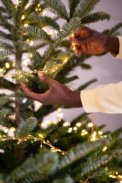 Uomo africano che decora l'albero di Natale dal vivo con un ragazzo nero ghirlanda a led che infila luci sull'abete