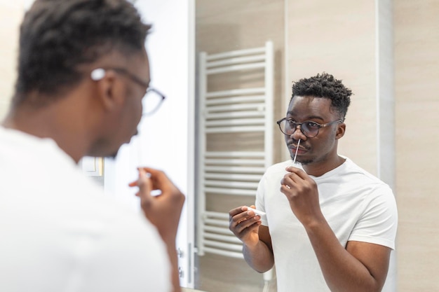Uomo africano che esegue l'autotest per COVID-19 a casa con il kit di test dell'antigene. Test del tampone nasale per l'infezione da coronavirus.