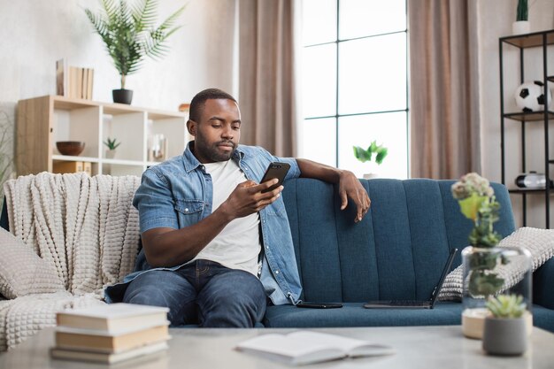 Uomo africano che parla al cellulare mentre si riposa sul divano