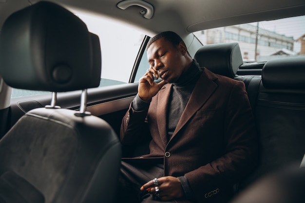 Uomo africano che utilizza smartphone mentre sedendosi sul sedile posteriore in automobile.