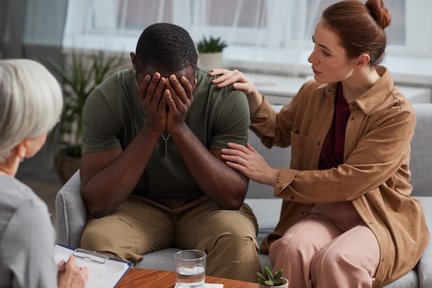 Uomo africano depresso che piange mentre ha una consultazione insieme a sua moglie che visitano lo psicologo
