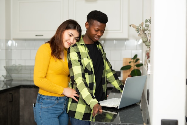 Uomo africano e donna asiatica in cucina con laptop