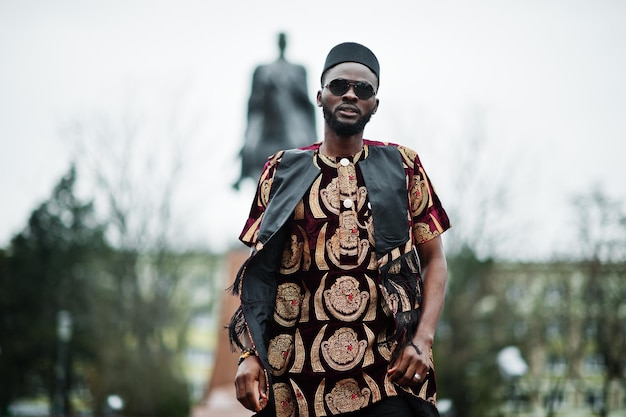 Uomo africano elegante e bello in abito tradizionale e berretto nero in piedi all'aperto.