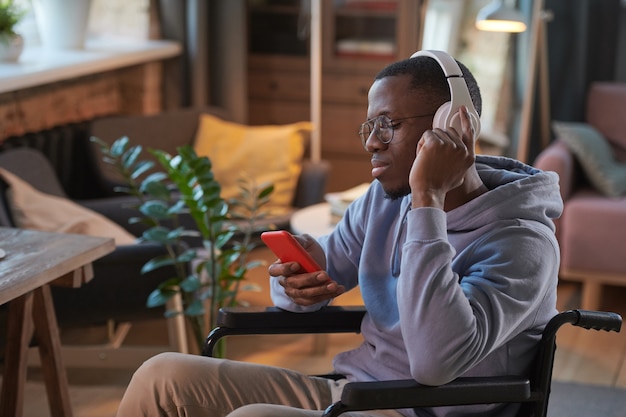 Uomo africano in cuffia usando il suo telefono cellulare mentre riposa a casa