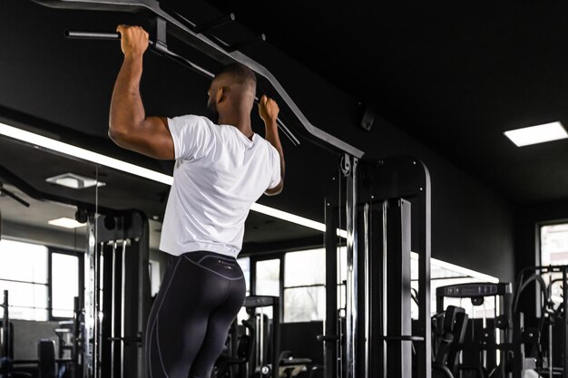 Uomo africano in forma e muscoloso che tira su la barra orizzontale in una palestra