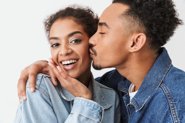 Uomo africano piacevole che bacia la sua amica sorridente sopra la parete grigia