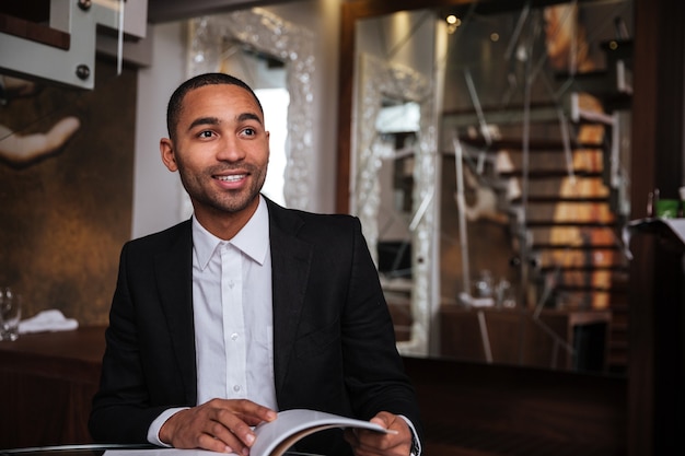 Uomo africano sorridente in completo con diario in hotel