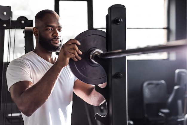 Uomo africano sportivo muscolare che aggiunge peso sul bilanciere in palestra