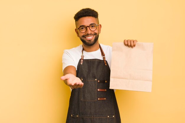 Uomo afro cool che sorride felicemente con amichevole e offrendo e mostrando un concetto di fattorino e fast food