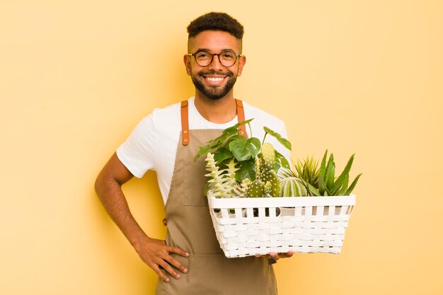 Uomo afro cool che sorride felicemente con una mano sull'anca e fiducioso giardiniere e concetto di pianta