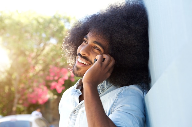 Uomo afro di risata che si appoggia contro la parete che parla sul telefono cellulare