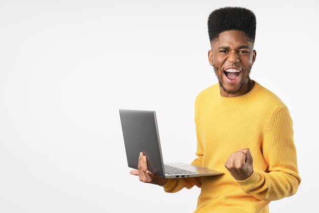 Uomo afro felice emozionante con il computer portatile che celebra la vittoria isolata sopra priorità bassa bianca