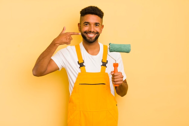 Uomo afro nero che sorride con sicurezza indicando il proprio concetto di casa di pittura con un ampio sorriso