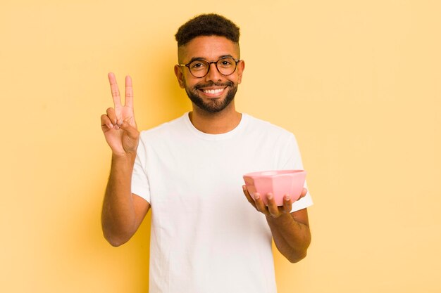 Uomo afro nero che sorride e sembra felice gesturing vittoria o pace concetto di ciotola vuota